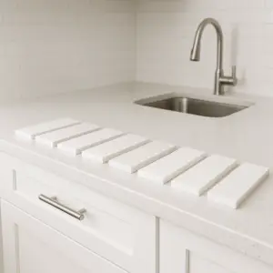 שיש לבן - למה זה עדיין הבחירה הכי פופולרית ב-2025? שמונה אריחים לבנים מלבניים מסודרים בשורה על משטח מטבח לבן, מול כיור עם ברז נירוסטה ואריחי מטרו לבנים.